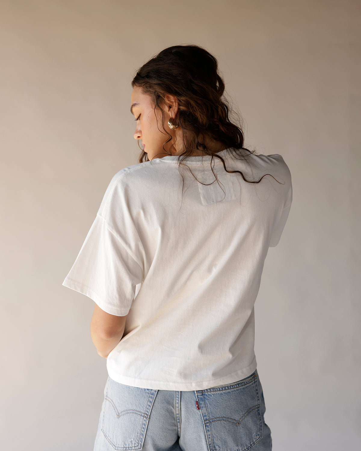 White oversized graphic tee worn from back, paired with light wash Levi's jeans