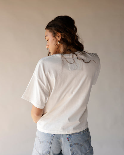 White oversized graphic tee worn from back, paired with light wash Levi's jeans