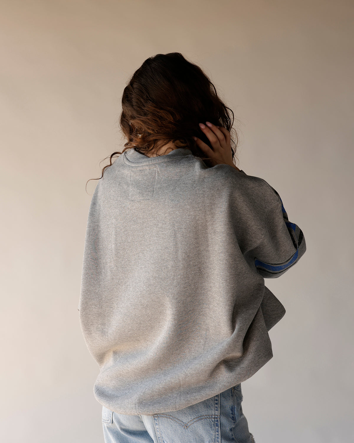 Gray crewneck sweatshirt with blue stripe sleeve detail, back view, worn with jeans