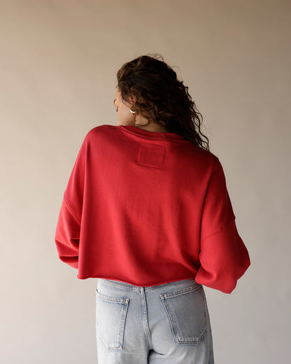 Red cropped crewneck sweatshirt with patch detail, back view, paired with light wash jeans