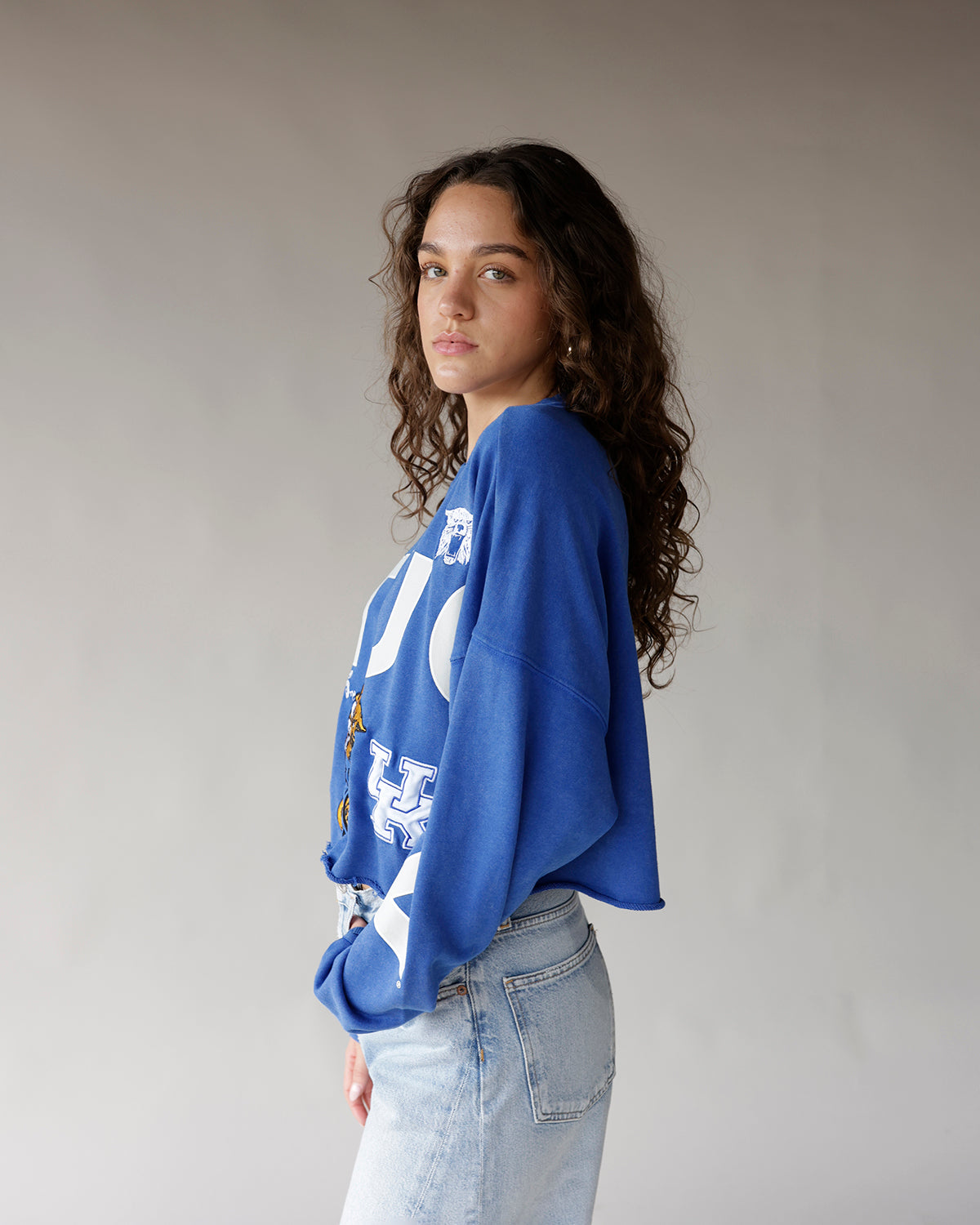 Blue cropped University of Kentucky graphic sweatshirt with white UK logo, worn with jeans