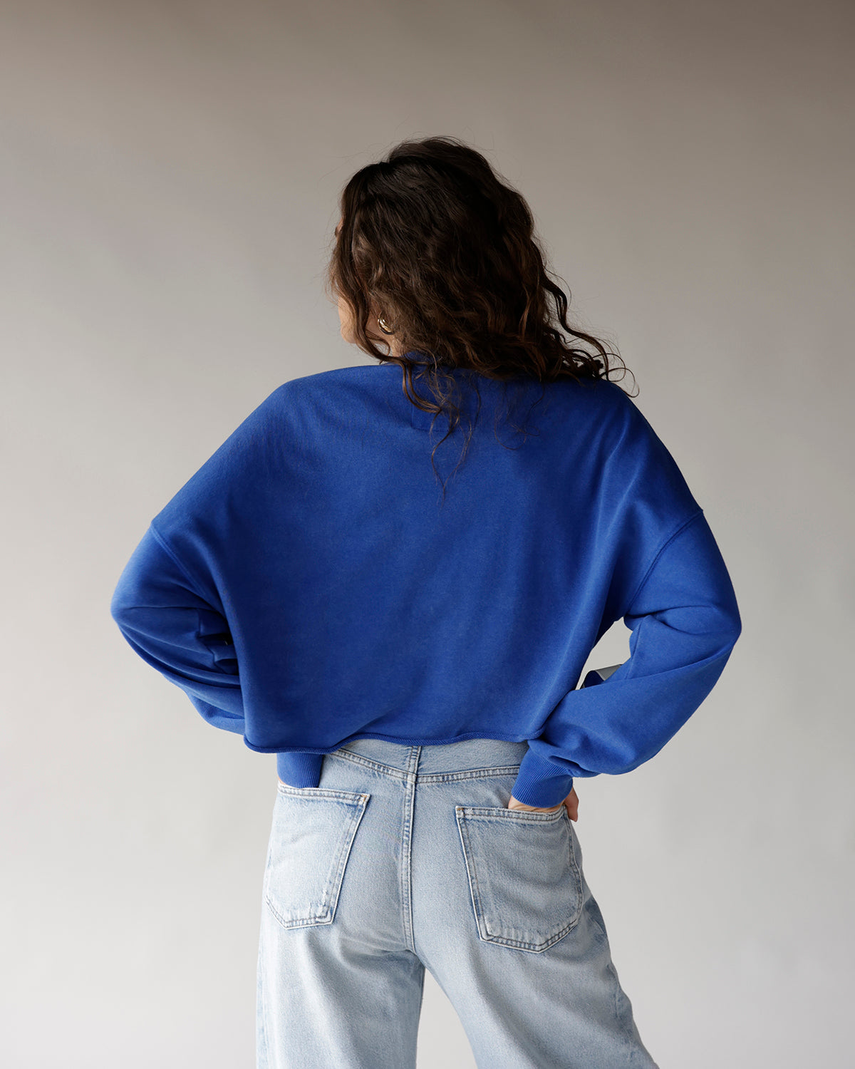 Oversized royal blue crop sweatshirt paired with light wash high-rise jeans, back view.