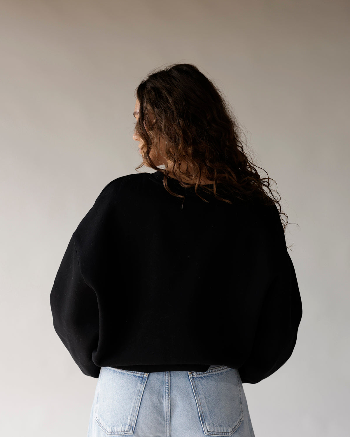 Black oversized crewneck sweatshirt back view, paired with light wash jeans