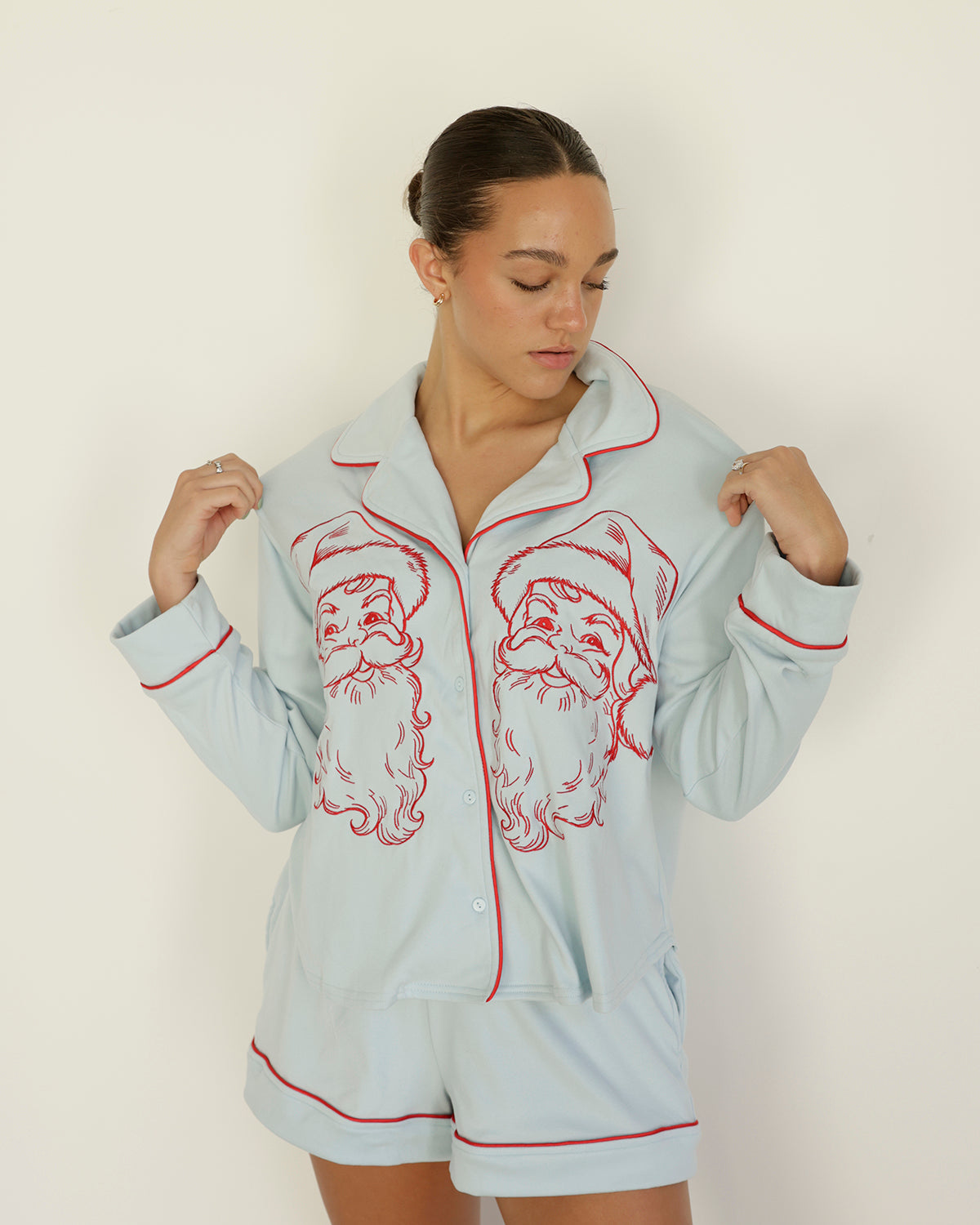 women's icy blue christmas pajama set featuring red vintage santa face illustrations, a long-sleeve button-down top with red piping, and matching shorts.