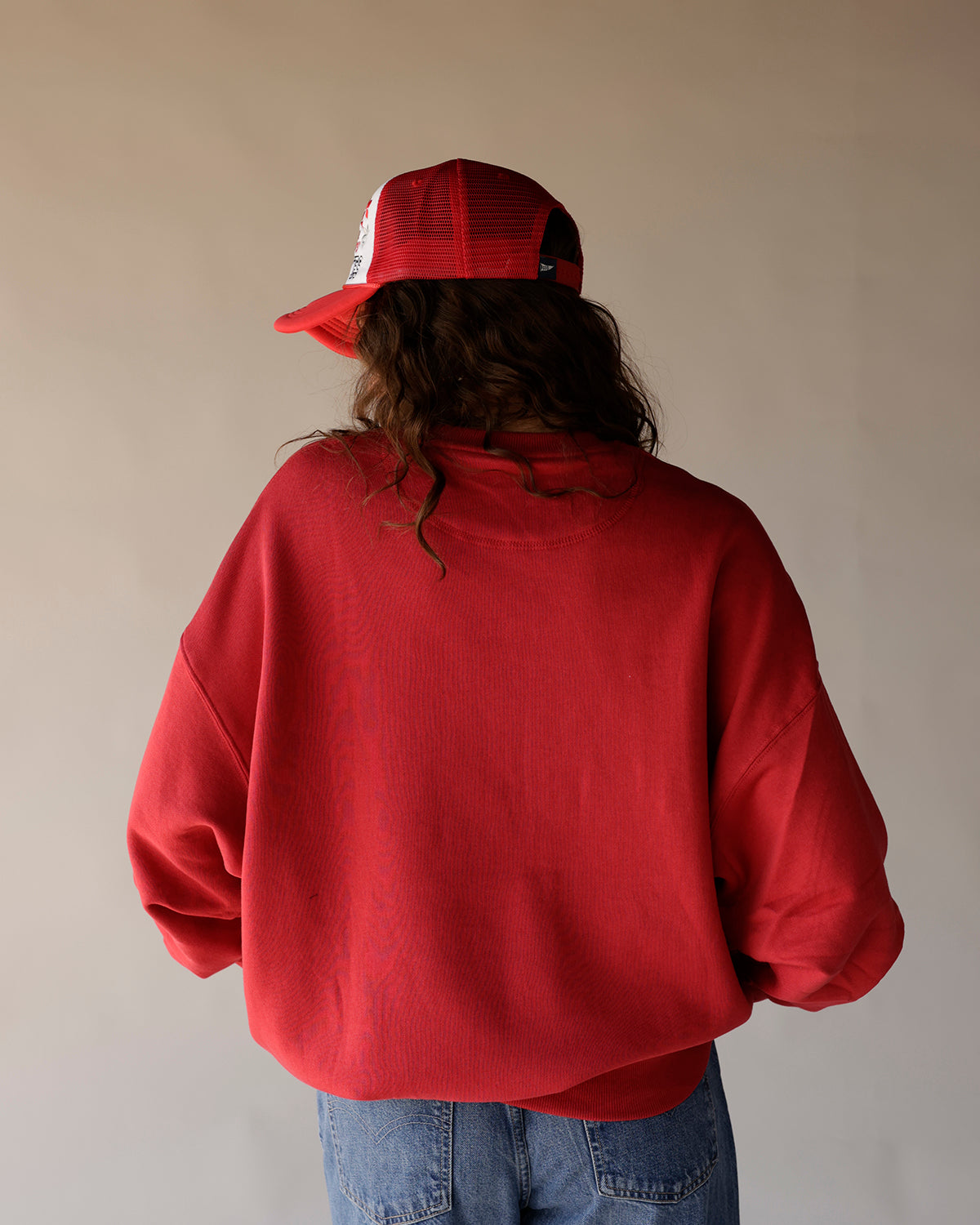 Red vintage crewneck sweatshirt shown from behind, paired with jeans and red trucker hat