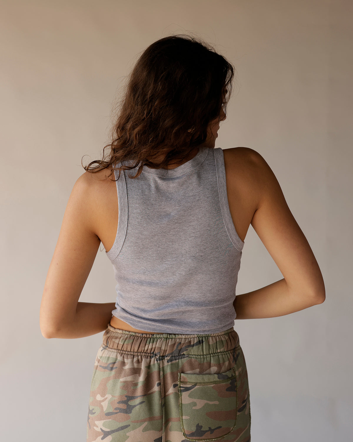 Gray racerback crop tank top, back view, worn with camo sweatpants