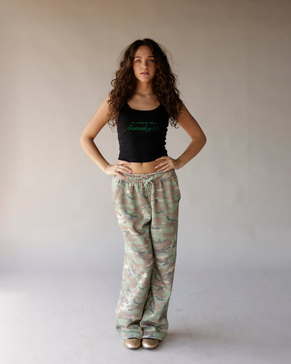 Black cropped tank top with green script graphic, styled with camo wide-leg sweatpants
