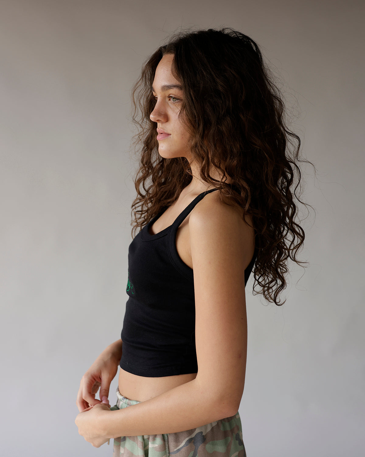 Black ribbed crop tank top with green embroidery, worn by woman with curly hair