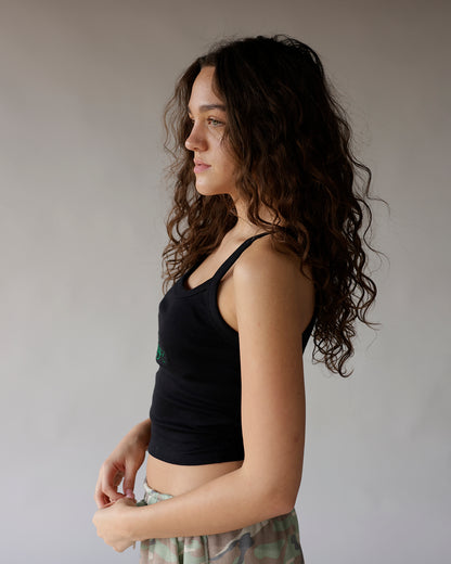 Black ribbed crop tank top with green embroidery, worn by woman with curly hair
