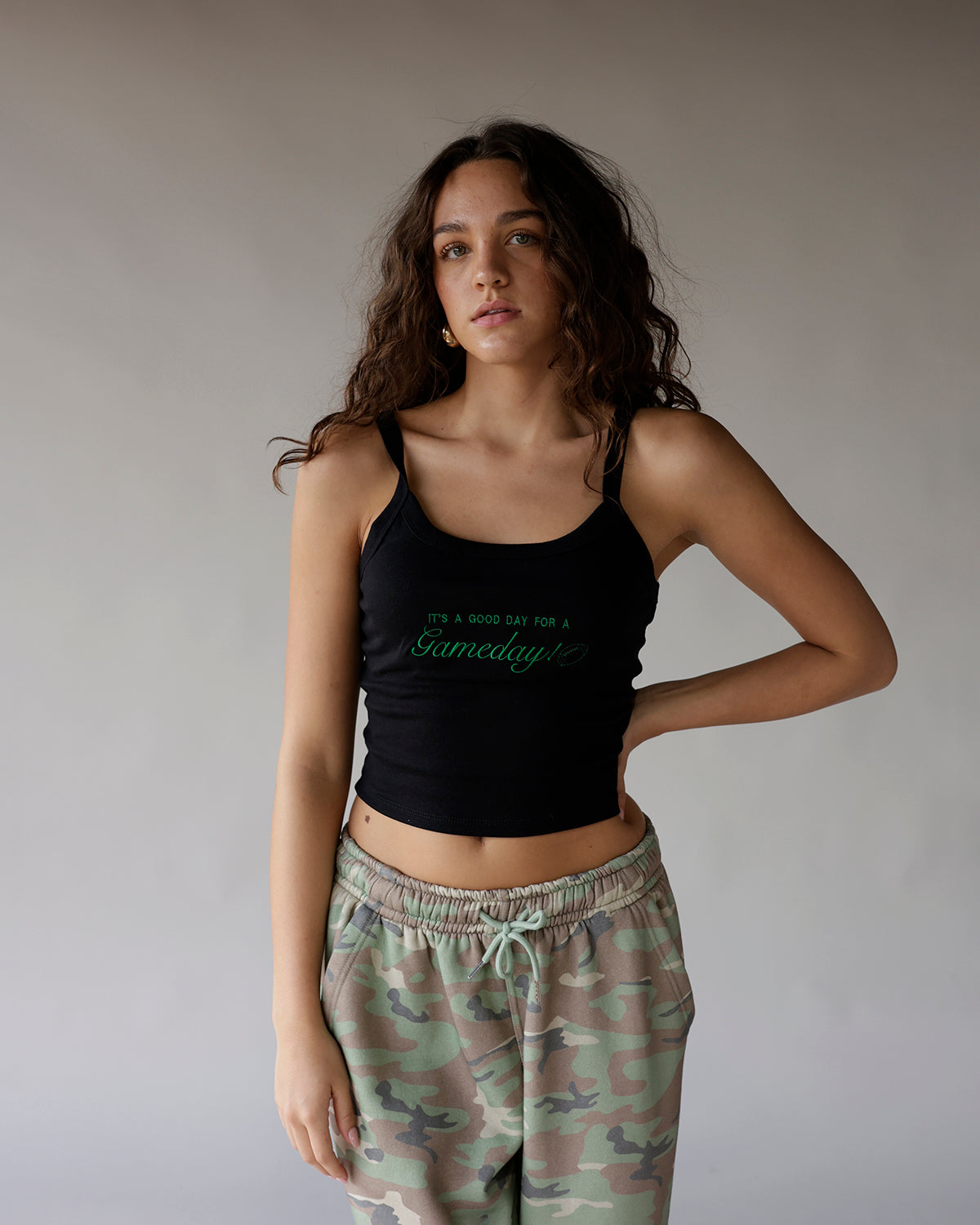 Black cropped tank top with green Gameday script graphic, worn with camo sweatpants