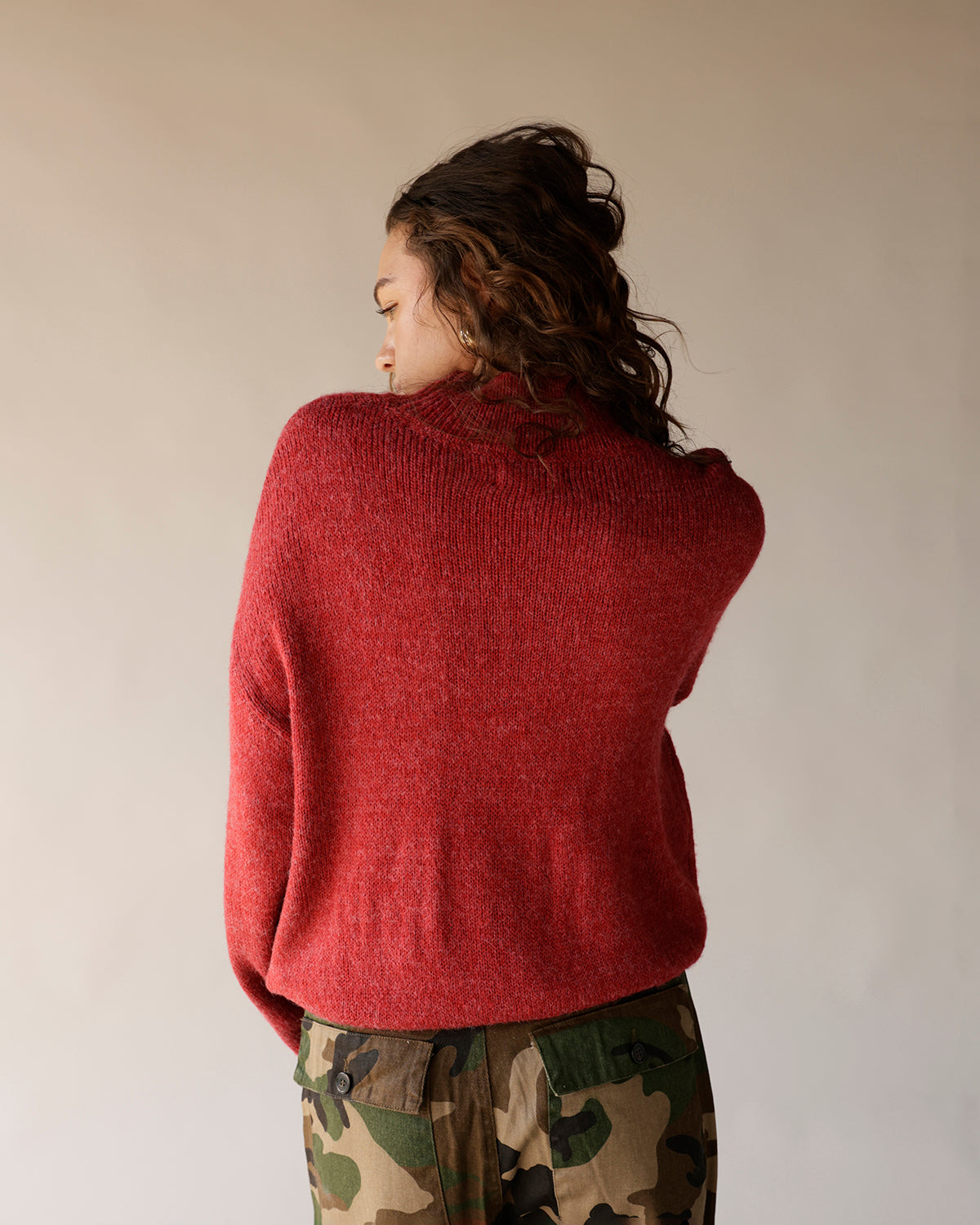 Oversized red heathered knit turtleneck sweater worn with camo cargo pants, back view.