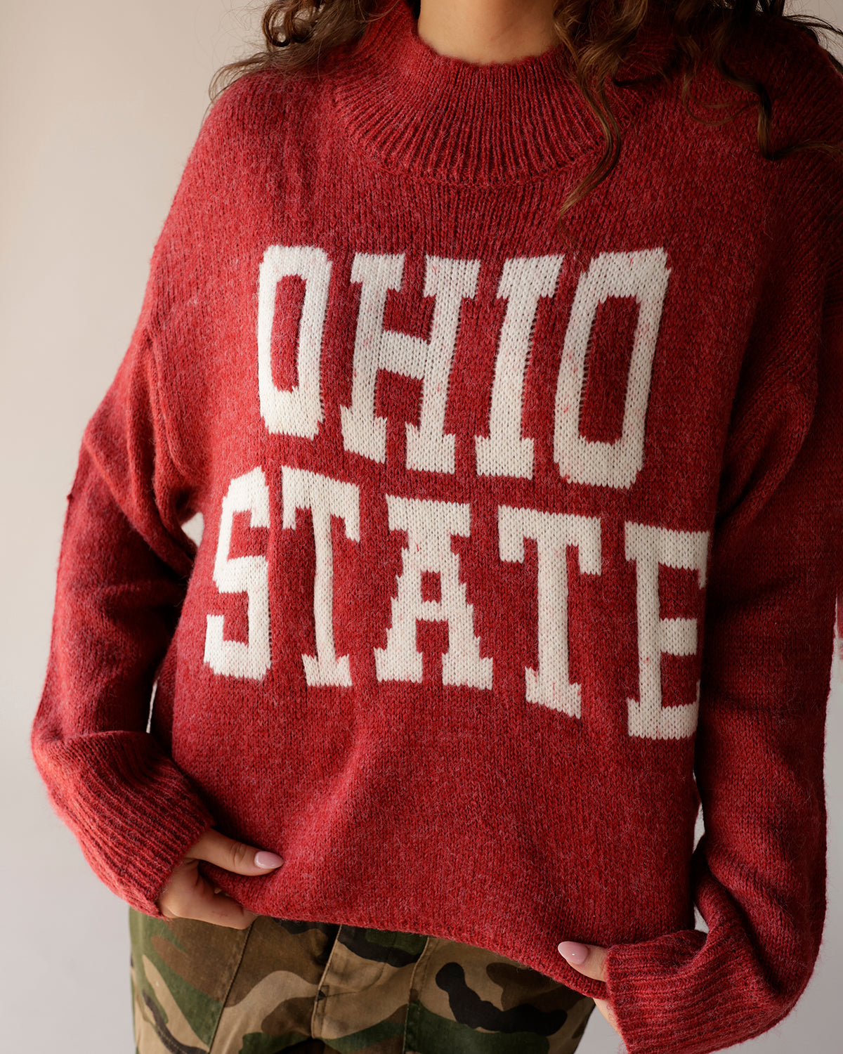 Red knit mock-neck sweater with bold white Ohio State lettering, worn with camo pants