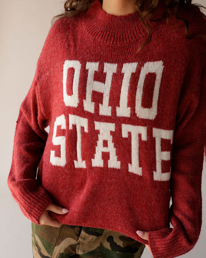 Red knit mock-neck sweater with bold white Ohio State lettering, worn with camo pants