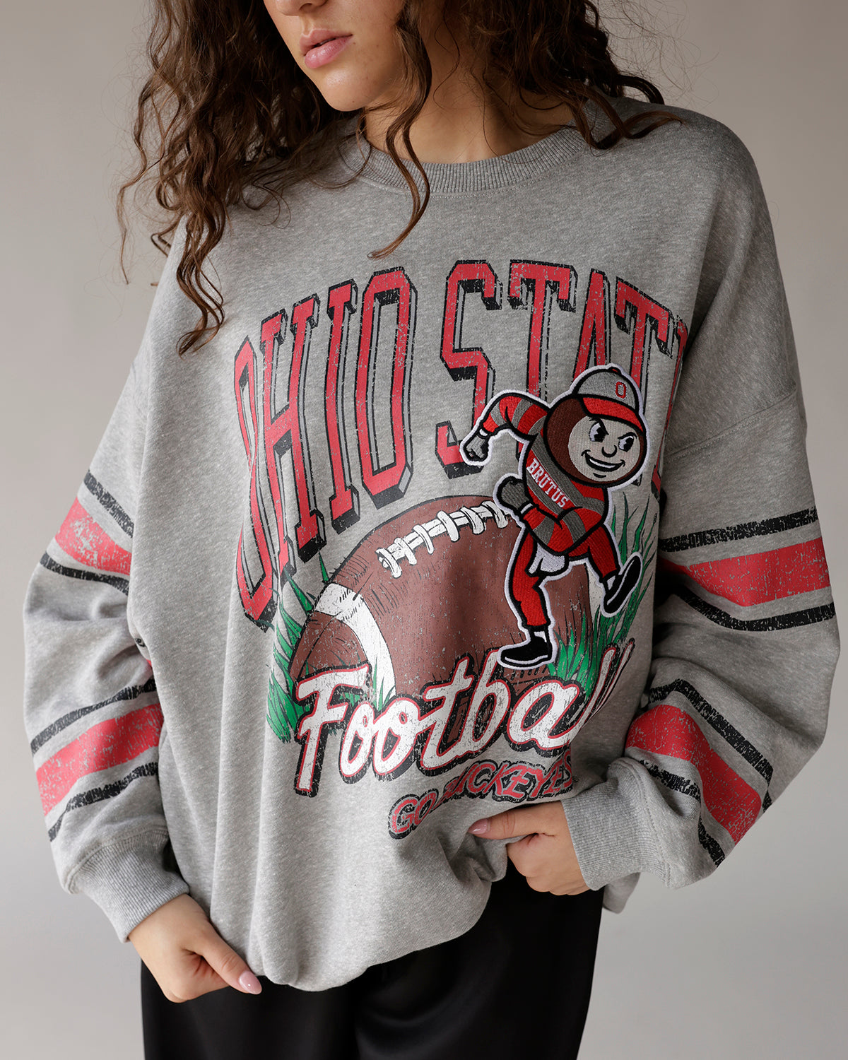 Gray Ohio State Buckeyes football crewneck sweatshirt with Brutus mascot graphic and striped sleeves