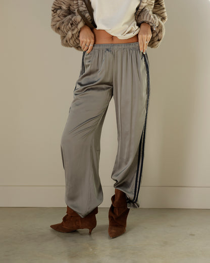 Loucia taupe-gray satin-look track pants featuring contrasting black double side stripes, an elastic waistband, side pockets and a relaxed wide-leg silhouette.