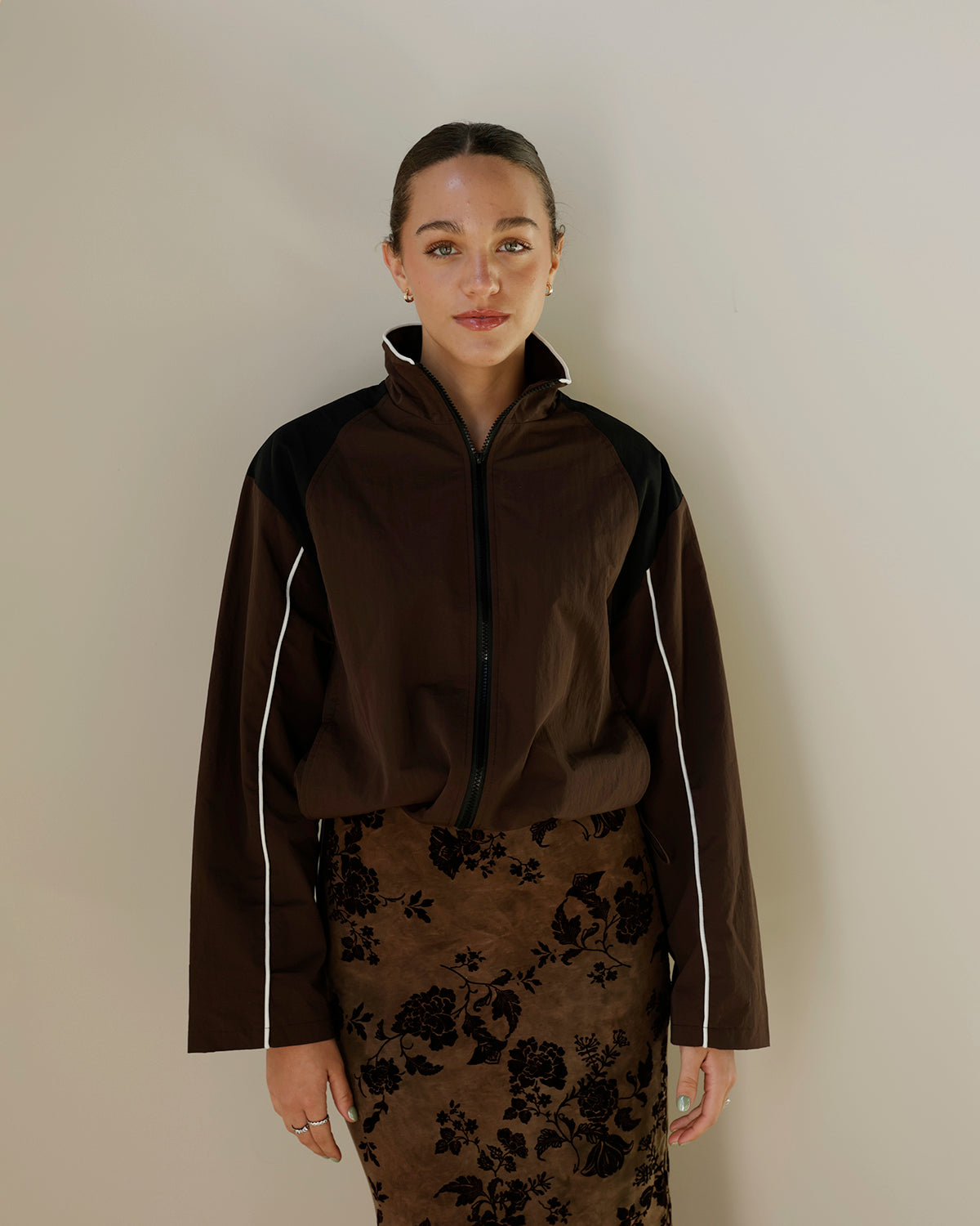 women's chocolate brown track jacket with black shoulder panels, white contrast piping, high stand collar, front zipper and relaxed boxy silhouette.