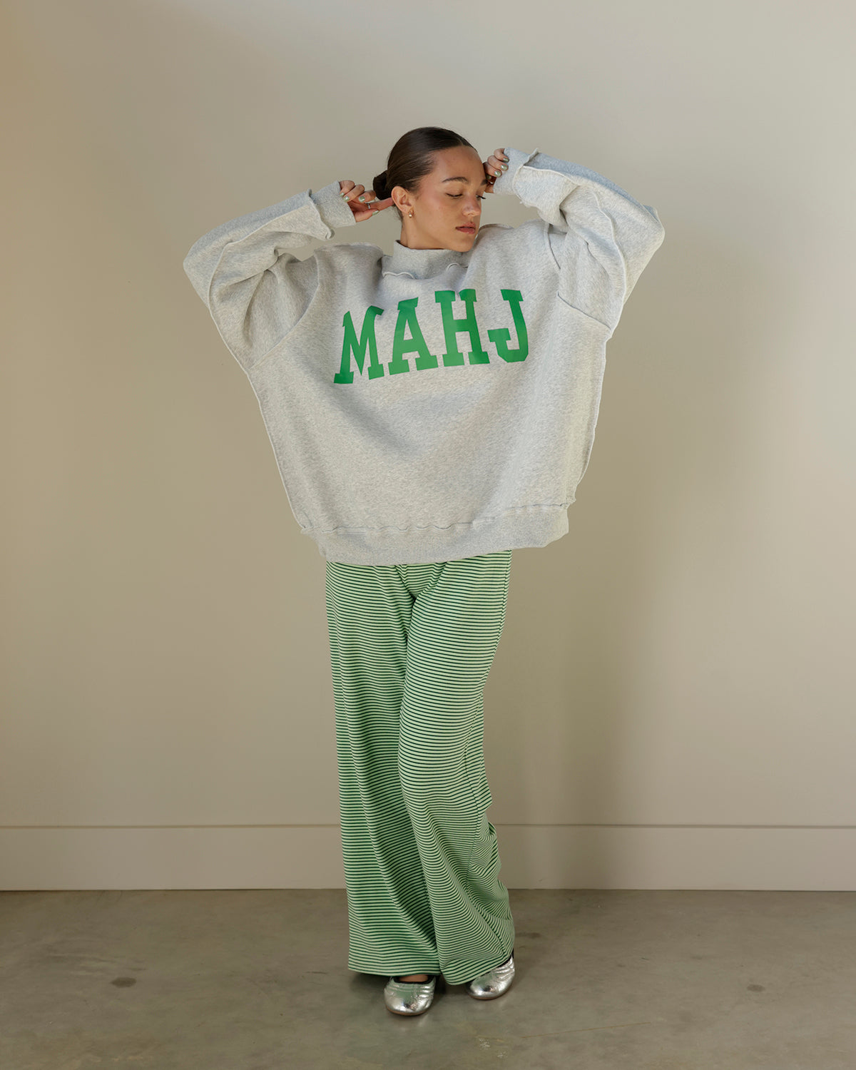 women wearing Mahj mockneck sweatshirt  and green striped lounge pants with silver ballet flats hair slicked back 