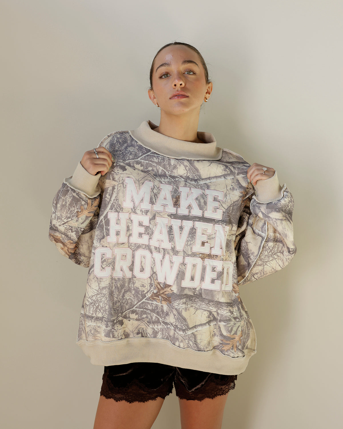 bucketlist make heaven crowded sweatshirt featuring neutral woodland camouflage, oversized cream varsity lettering, oatmeal mock neckline and ribbed trim.