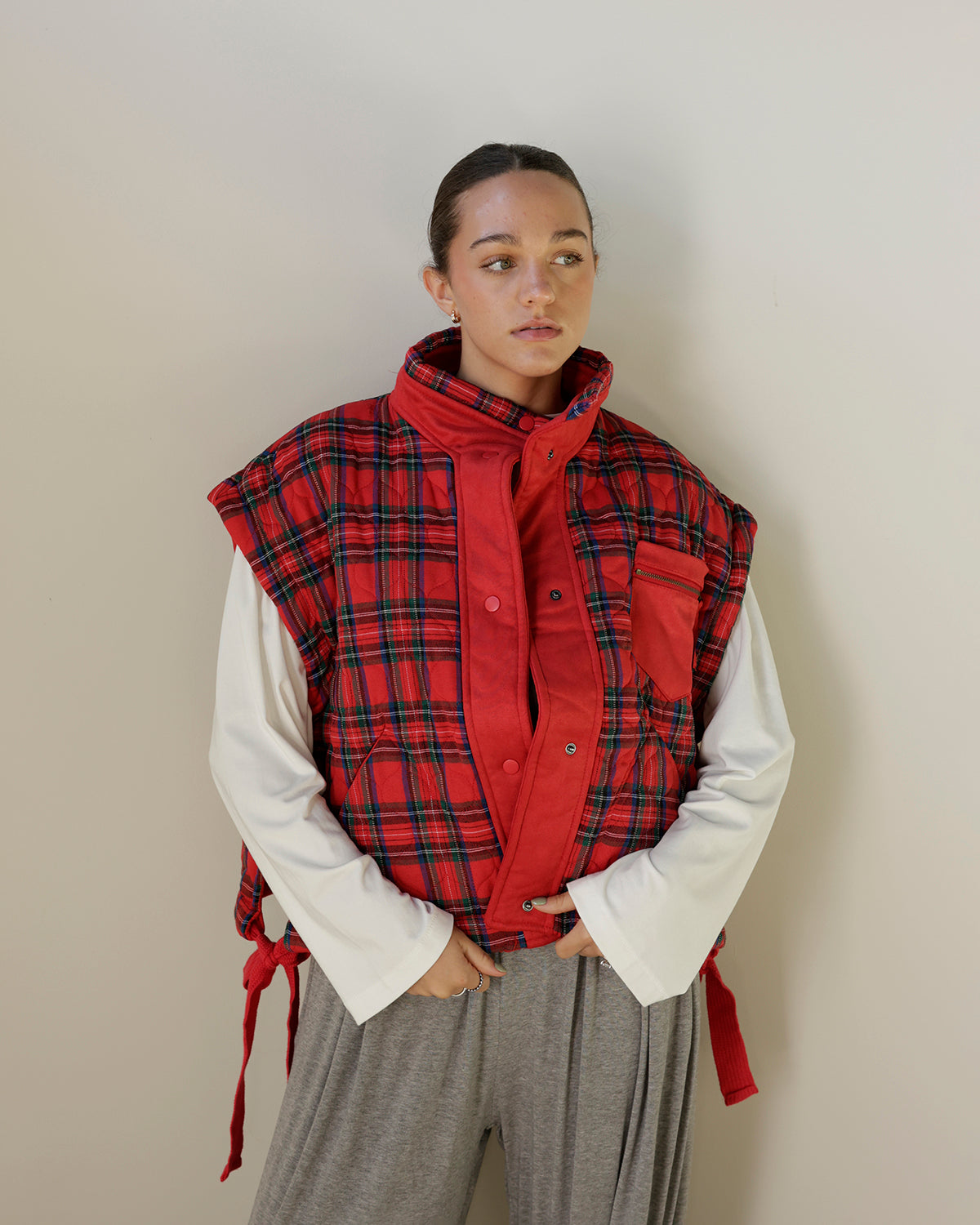 red tartan plaid sleeveless utility vest featuring a contrasting red stand collar, snap-front closure, zippered chest pocket and adjustable side ties.