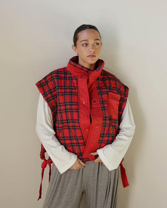 red tartan plaid sleeveless utility vest featuring a contrasting red stand collar, snap-front closure, zippered chest pocket and adjustable side ties.