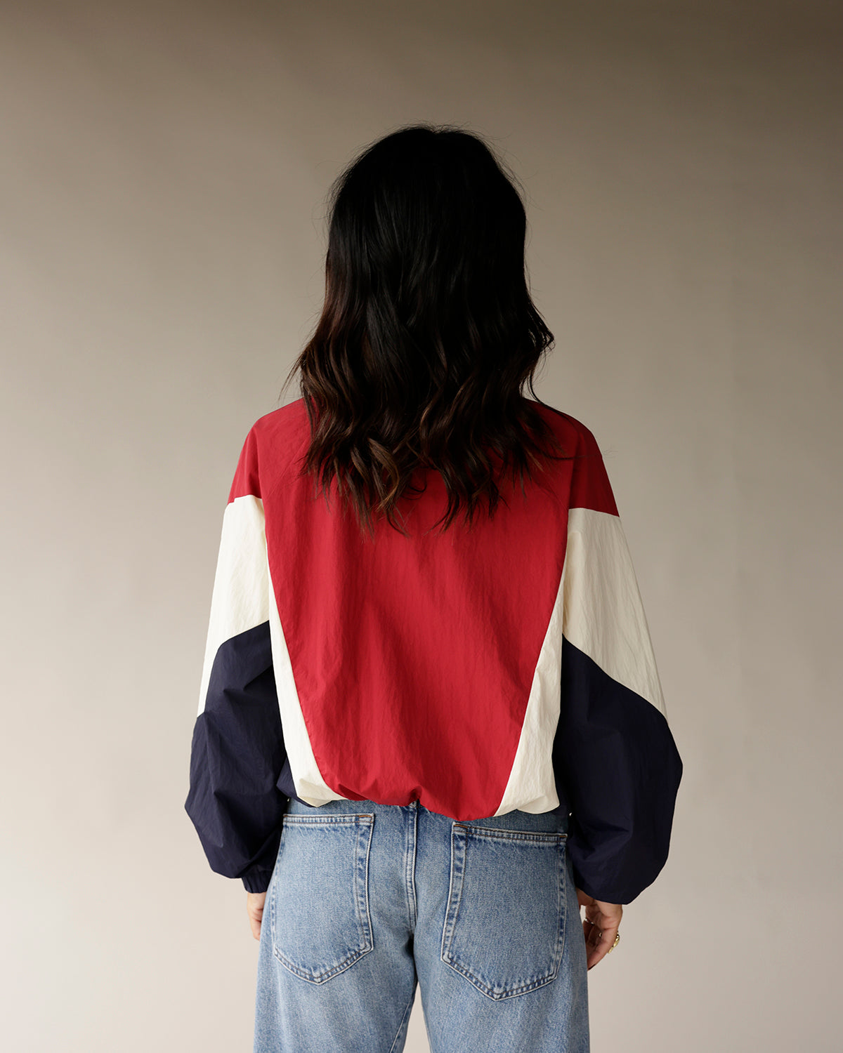 Red, navy, and cream colorblock retro windbreaker jacket, back view, paired with jeans.