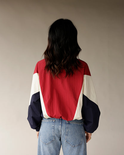 Red, navy, and cream colorblock retro windbreaker jacket, back view, paired with jeans.