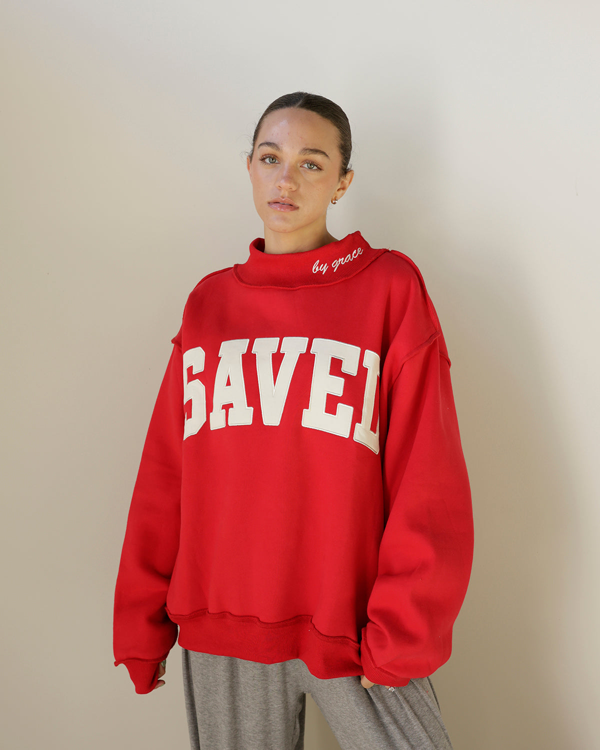 shop the bucketlist saved by grace sweatshirt in bold red with cream varsity lettering, mock neckline and an oversized fit. faith-inspired style with attitude.