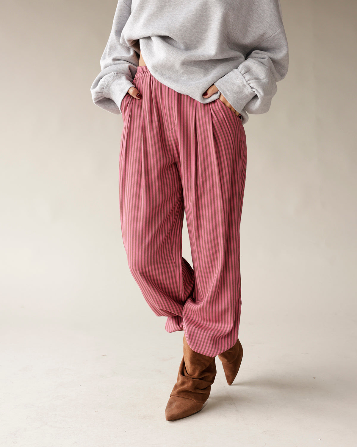 Pink striped relaxed-fit pleated trousers with elastic waist, styled with brown boots