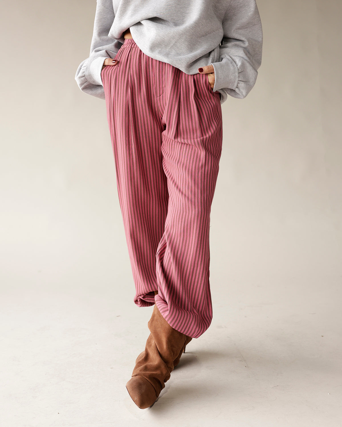Pink striped wide-leg pleated trousers with elastic waist, styled with brown boots
