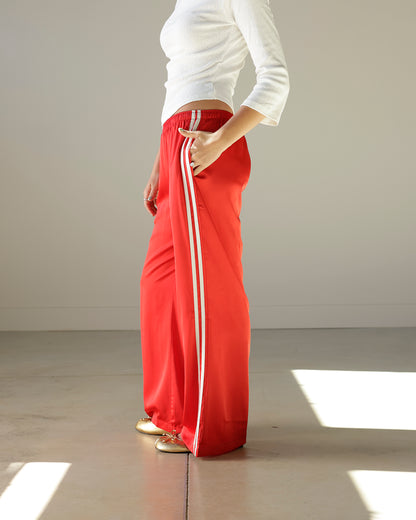 Loucia cherry red satin-look track pants featuring contrasting ivory side stripes, an elastic waistband, side pockets and a relaxed wide-leg silhouette.