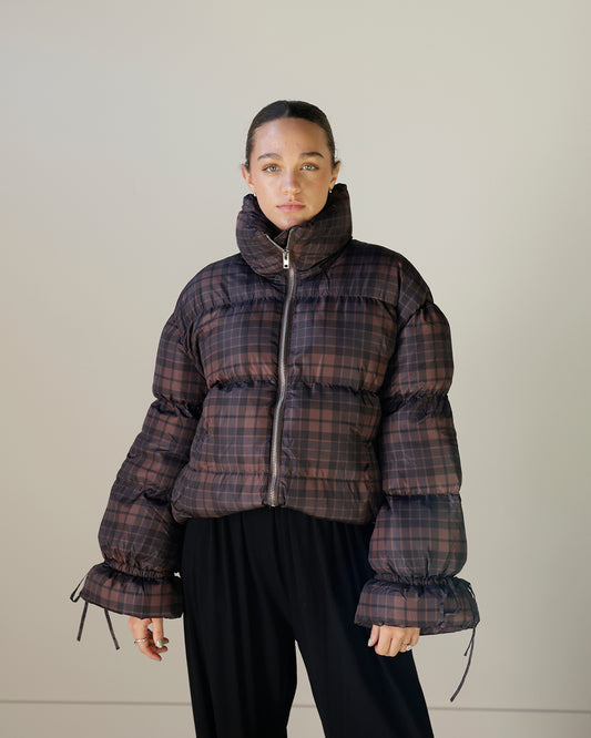 women's chocolate brown and black plaid puffer jacket with an oversized cropped silhouette, high stand collar, full zipper and voluminous tie-cuff sleeves.