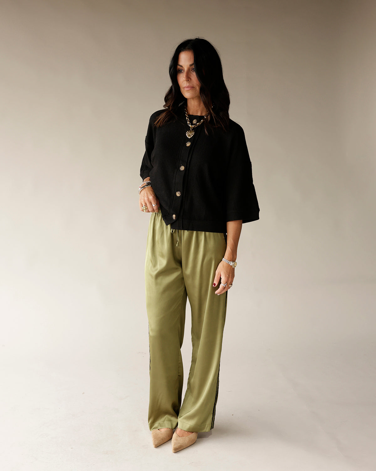 Black cropped button-front cardigan with gold buttons worn over olive wide-leg pants