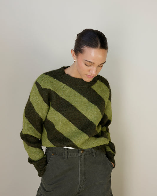 women wearing slanted horizontal striped green sweater and jeans, hair pulled back 
