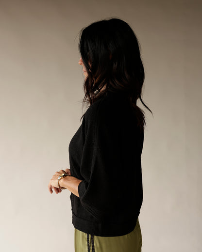 Women's black ribbed knit pullover sweater with 3/4 sleeves, side profile view