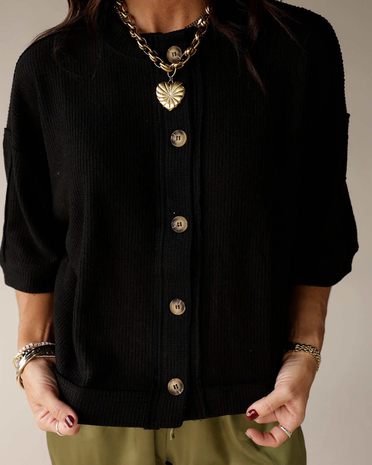 Black ribbed knit short-sleeve button-front cardigan with gold heart pendant necklace