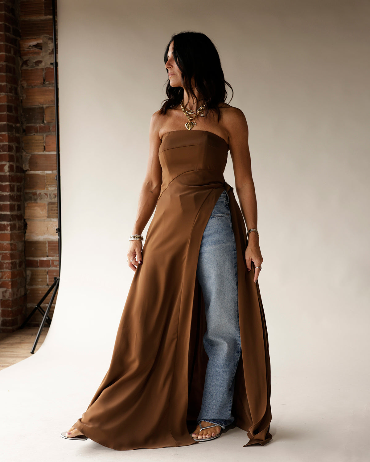 Brown strapless maxi tunic with high slit, worn over wide-leg jeans