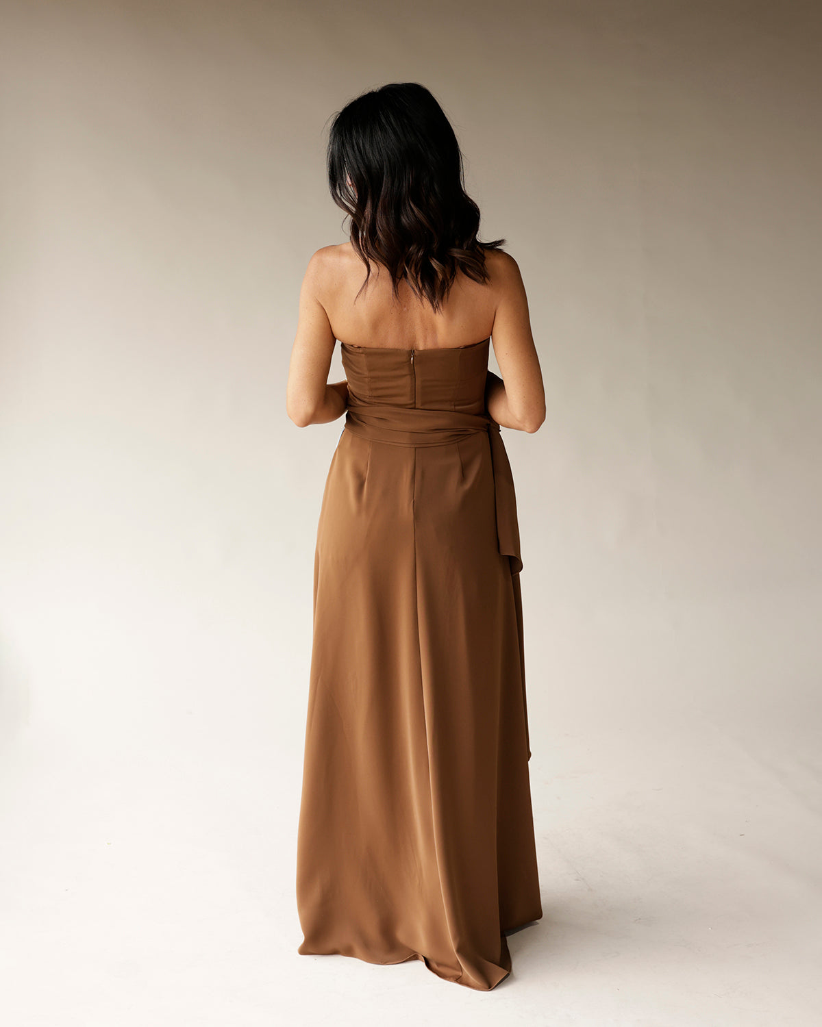 Brown strapless satin maxi dress with waist tie, back zipper, shown from behind