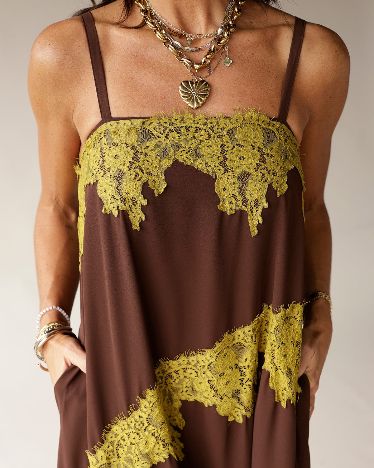 Brown slip dress with yellow-green lace trim detail, spaghetti straps, and layered gold necklaces