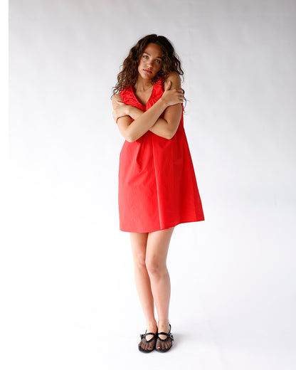 Red sleeveless mini dress with ruffle V-neckline, A-line silhouette, worn with black sandals.
