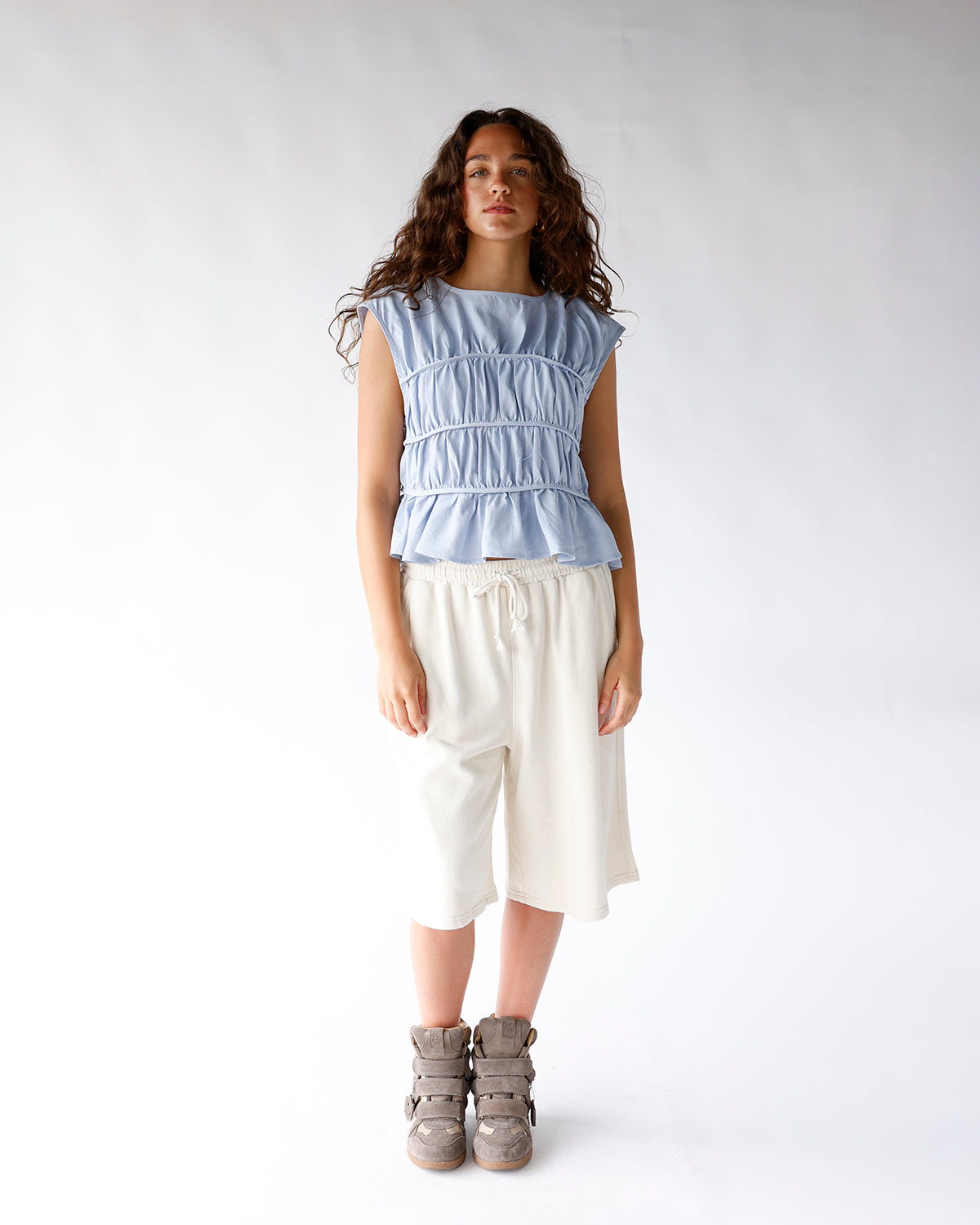 Light blue sleeveless ruched top with tiered peplum hem, worn with cream shorts