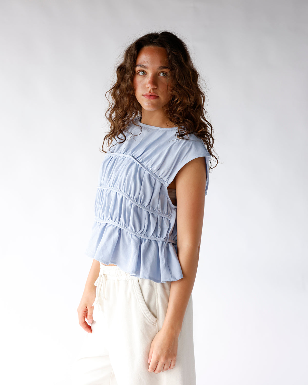 Light blue ruched sleeveless crop top with diagonal pleating and peplum hem