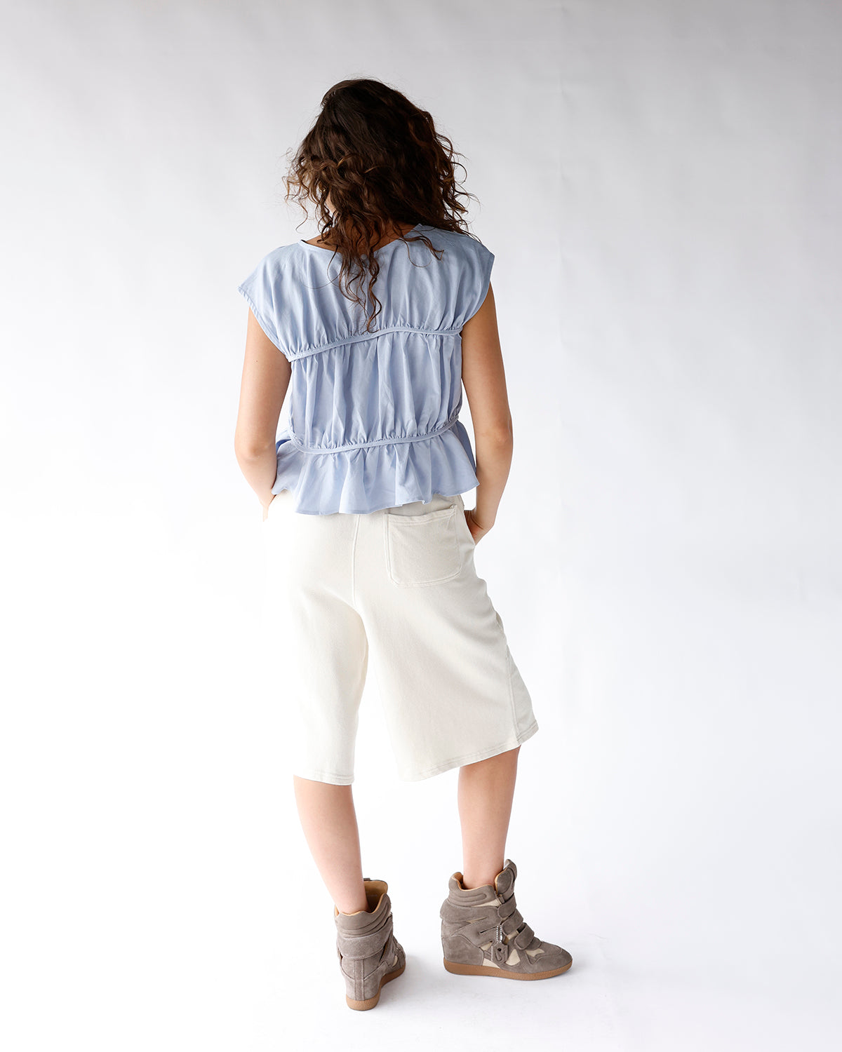 Light blue sleeveless ruched peplum top with gathered waist detail, back view