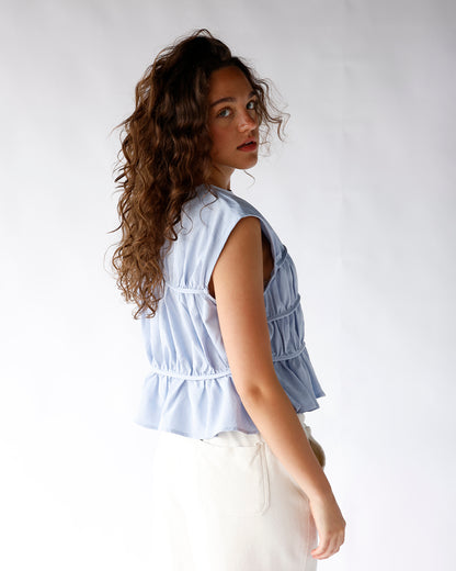Light blue sleeveless tiered peplum top with ruched detailing, paired with white pants
