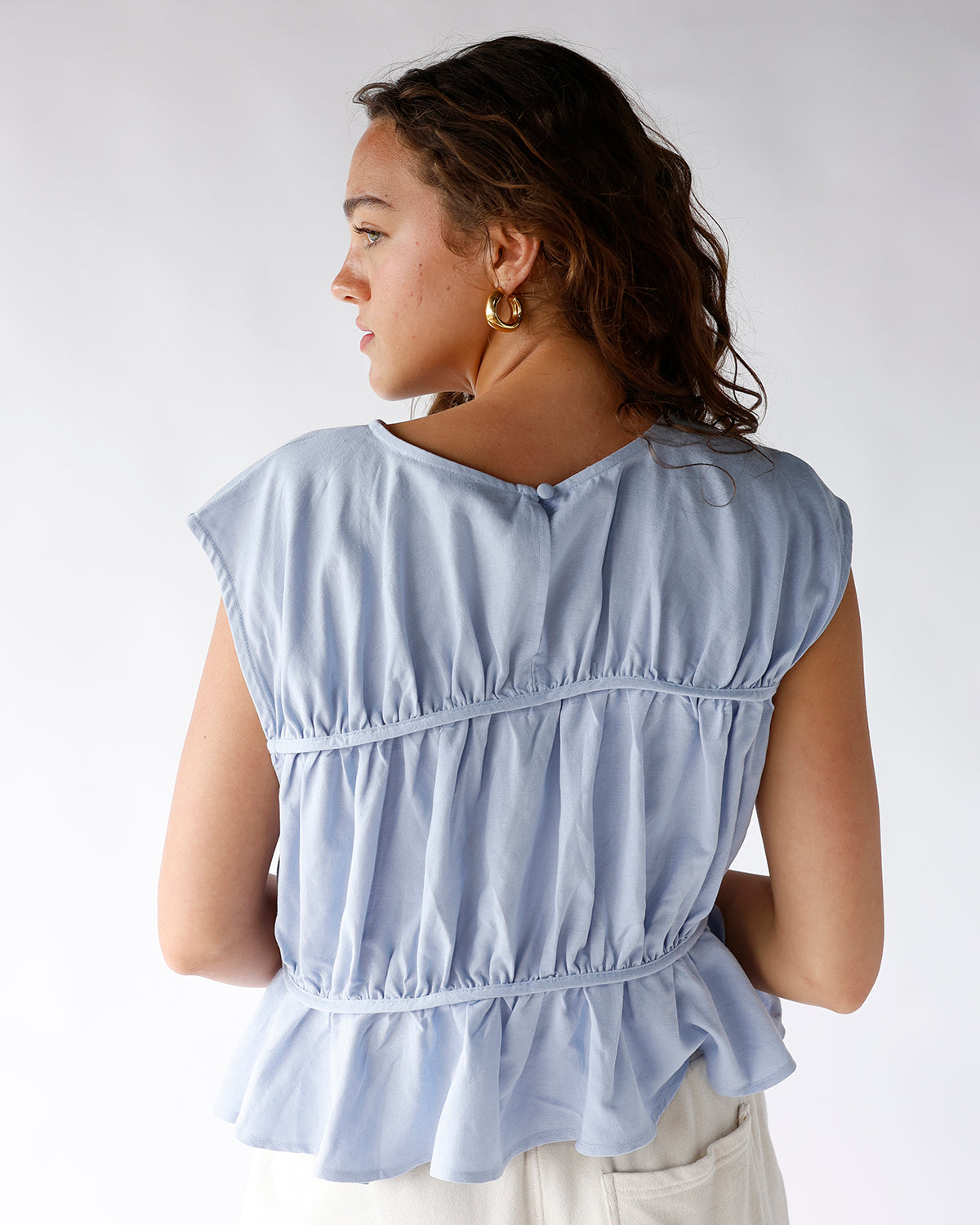 Light blue sleeveless peplum top with ruched tiers and button back detail