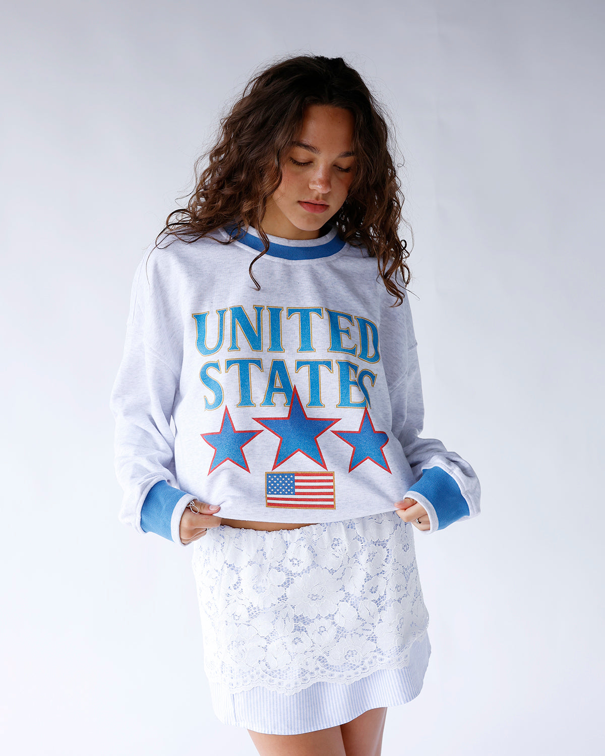 United States sweatshirt featuring blue outlined gold lettering, red-outlined stars, American flag detail, and blue-gray trim. A cozy patriotic pullover perfect for everyday wear and holidays.