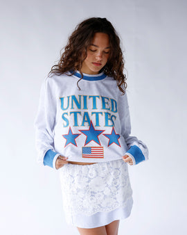 United States sweatshirt featuring blue outlined gold lettering, red-outlined stars, American flag detail, and blue-gray trim. A cozy patriotic pullover perfect for everyday wear and holidays.
