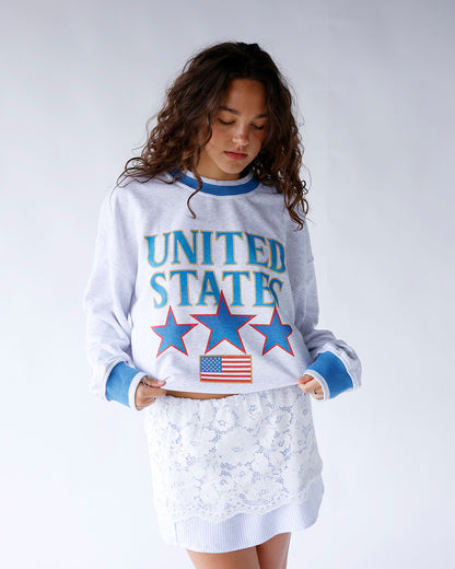 United States sweatshirt featuring blue outlined gold lettering, red-outlined stars, American flag detail, and blue-gray trim. A cozy patriotic pullover perfect for everyday wear and holidays.