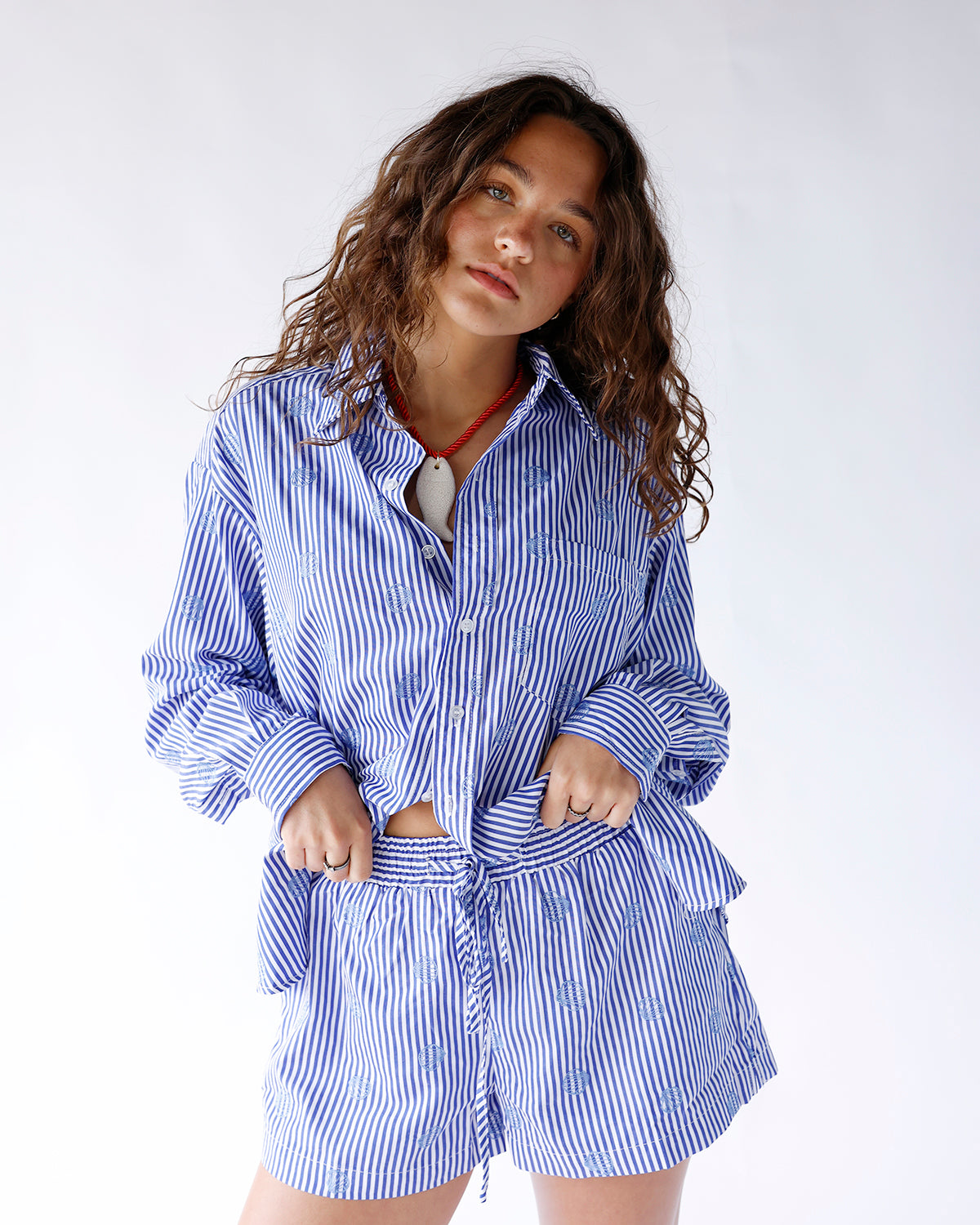 Blue and white striped button-up shirt featuring delicate blue seashell embroidery throughout. A classic coastal-inspired top perfect for beach vacations and effortless everyday styling.