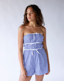 Blue and white striped strapless romper featuring blue seashell embroidery and three vertical white bows. A cute coastal-inspired one-piece perfect for summer and vacation wear.