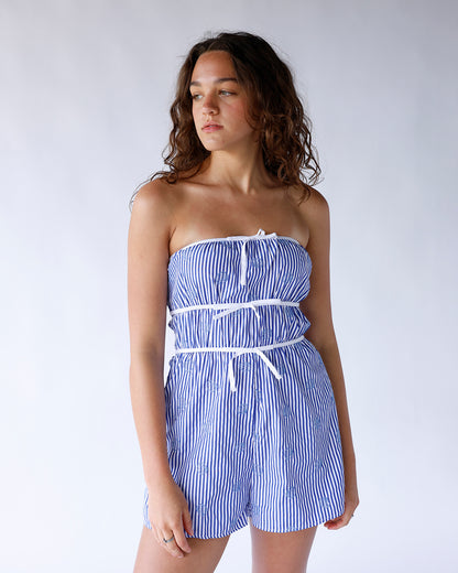 Blue and white striped strapless romper featuring blue seashell embroidery and three vertical white bows. A cute coastal-inspired one-piece perfect for summer and vacation wear.
